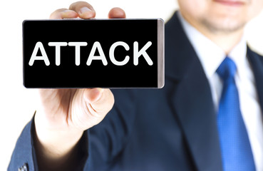 ATTACK word on mobile phone screen in blurred young businessman hand over white background, business concept