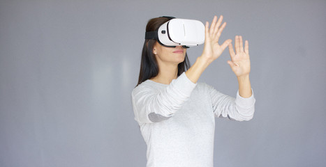 Long haired beautiful woman playing with Virtual Reality 3D glasses while isolated on gray background. She doing gestures with her hands.