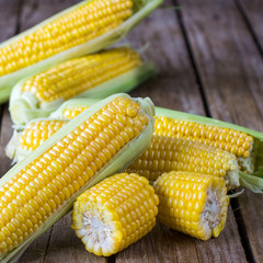 A whole fresh corn and pieces of corn on the wooden table