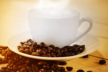 Coffee cup and coffee beans with steam on wooden table background, Close-up and golden tone.