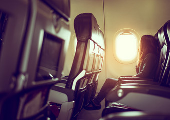 Naklejka premium Lady is sitting in airplane looking out at bright sky through wi