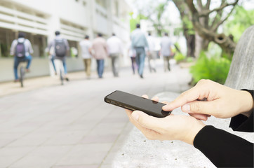 Businessman is using mobile phone to do something over blurred background of crowded walking people in a university