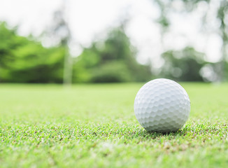 Golf ball on green with blurred pin flagstick and green tree background