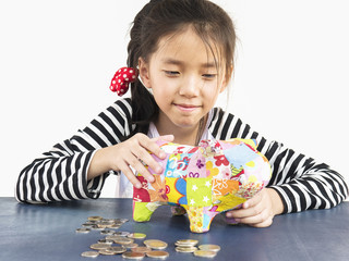 Asian kid is putting money in to a colorful piggy coin bank