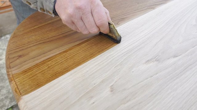 Carpenter is covering wooden table by lacquer. Worker making furniture and toning wood by paint