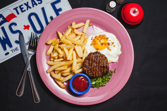 beefsteak with fried potatoes and eggs on a plate, top view