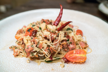 Spicy spaghetti with bacon and basil in the white dish.
