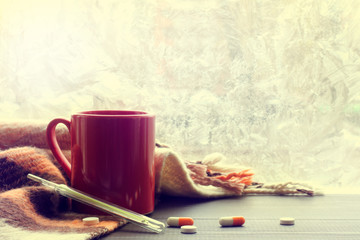 warming drinks for colds/ pellets tablets and mercury thermometer with red mug in blankets and background of frozen window