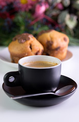 Morning coffee in black cup with muffins behind.