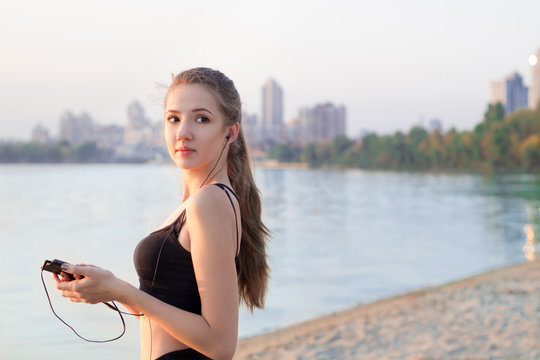 Fitness woman at lake listening to music on mobile phone