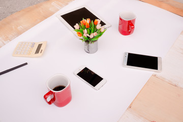 Desktop Mix of office supplies and gadgets View from above. white desk with Smart Phone,notebook,tablet,calculator,cup of Coffee and Measurement Tool On a white table.