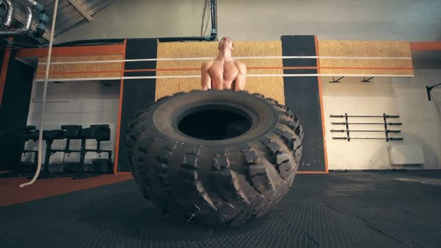 Strong muscular young man flipping tyre while exercising in CrossFit gym.