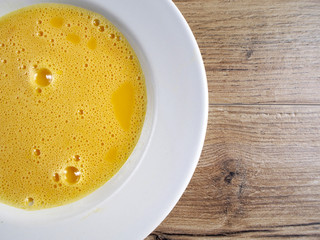 Beaten egg in old plate on wood background