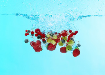 Berries falling into water on color background