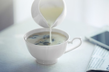 Pouring milk in tea on table