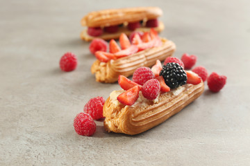 Delicious eclairs with berries on light textured background