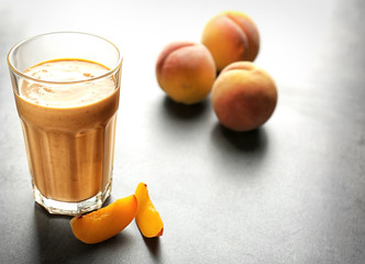 Glass with tasty smoothie and peach on grey table
