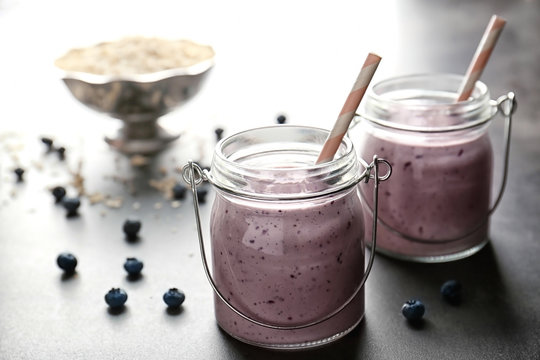 Two mason jars with tasty smoothie and straws on grey table