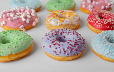 Tasty donuts with colorful sprinkles on light background