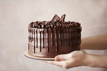Woman holding tasty chocolate cake on grey background