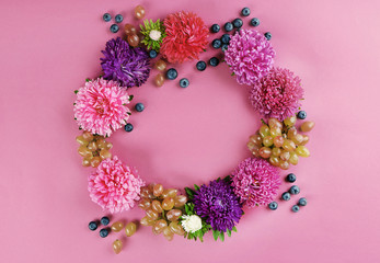 Beautiful wreath with flowers, grape and blueberry on pink background