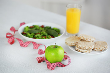 Measuring tape with green apple and vegetable salad on table
