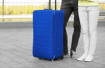 Young travelers walking with big blue trunk on street, closeup