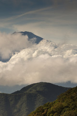 Hakone, Japan - September 27, 2016: Portrait of the summit of mount Fuji visible and peeking through bands of rainy clouds as it is seen from Mount Komagatake. Forest in foreground.