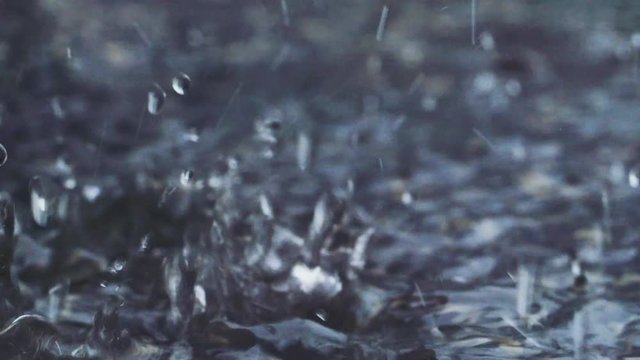 Heavy rain on water shot with high speed camera. Slow motion close up shot of falling rain drops and water bubbles. Wet asphalt on the street. Stormy, rainy, nasty wether.