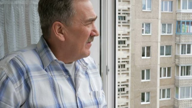Elderly man with a mustache smoking on the balcony. One can see the multi-storey panel home. Thoughtful look into the distance