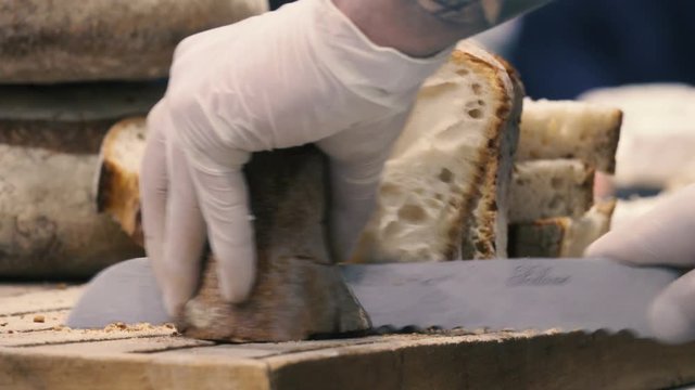 Baker cuts bread on a cutting board, close-up, blurred background