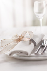 Fototapeta na wymiar Beautifully elegant decorated table for holiday - wedding or valentine day with modern cutlery, bow, glass, candle and gift, closeup, toned