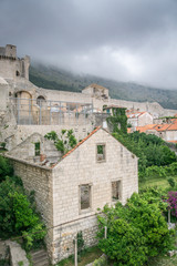 Fototapeta na wymiar Ominous storm clouds cover Mount Srd, which sits behind the old town of Dubrovnik, Croatia, with war damaged buildings visible in the foreground, and the city walls and fortifications visible in the b