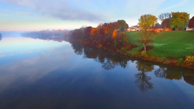 Scenic riverside small town with foggy Autumn sunrise, aerial flyover.
