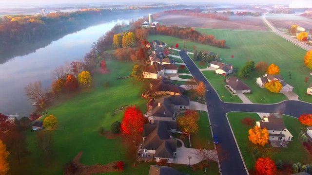Scenic riverside small town with foggy Autumn sunrise, aerial flyover.
