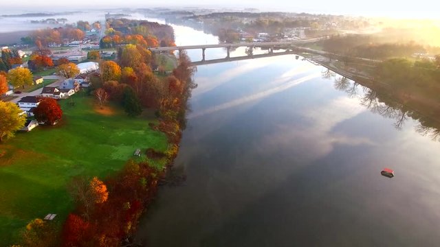 Scenic riverside small town with foggy Autumn sunrise, aerial flyover.
