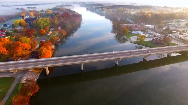 Scenic riverside small town with foggy Autumn sunrise, aerial flyover.
