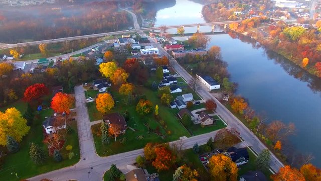 Scenic riverside small town with foggy Autumn sunrise, aerial flyover.
