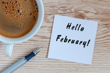 hello February on peace of paper near morning coffee cup at workplace background