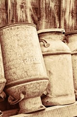 Sepia vintage milk cans leaning against a barn.  Grungy texture.