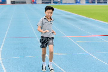 Obraz premium Young Asian boy running on blue track in the stadium