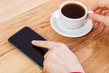 Hand of woman touching blank screen of mobile phone, cup of coffee