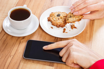 Hand of woman using mobile phone, oatmeal cookies and cup of coffee