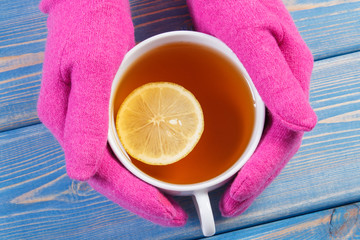 Hand of woman in woolen gloves holding cup of hot tea on table