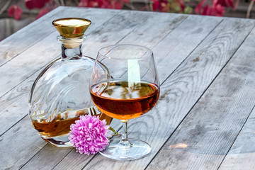 Bottle and snifter brandy with flower on table in garden