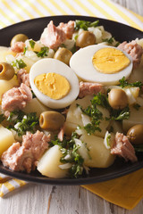 Spanish cuisine: boiled potatoes with tuna, eggs, olives dressed with sauce closeup. vertical