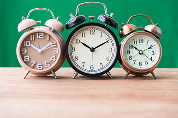 three alarm clock on wooden table with green background