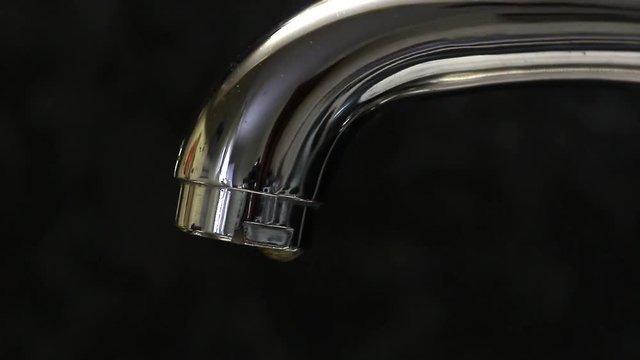 Water drips from a faucet close-up on a black background.
