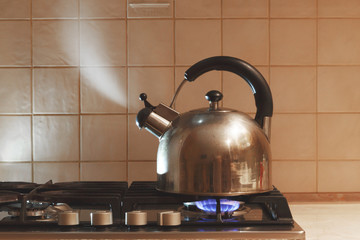 Water boils in a metal teapot on a gas stove.