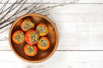 Ripe Persimmon fruit in a wooden bowl with willow twigs